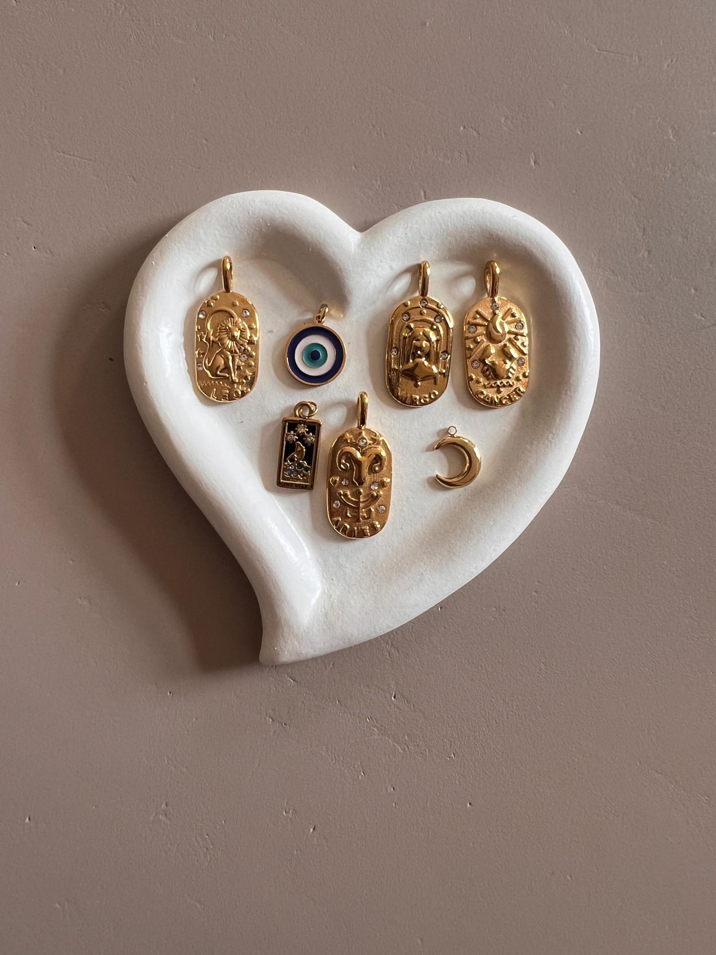 Gouden bedels met sterrenbeelden, evil eye en maantje in een hartvormig schaaltje