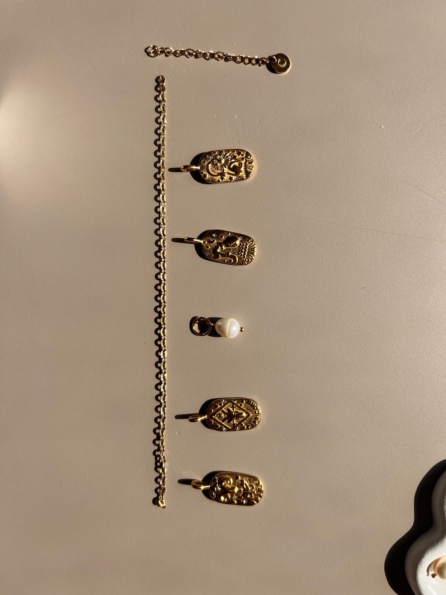 Gouden ketting met sterrenbeeld-bedels en een zoetwaterparel in het zonlicht