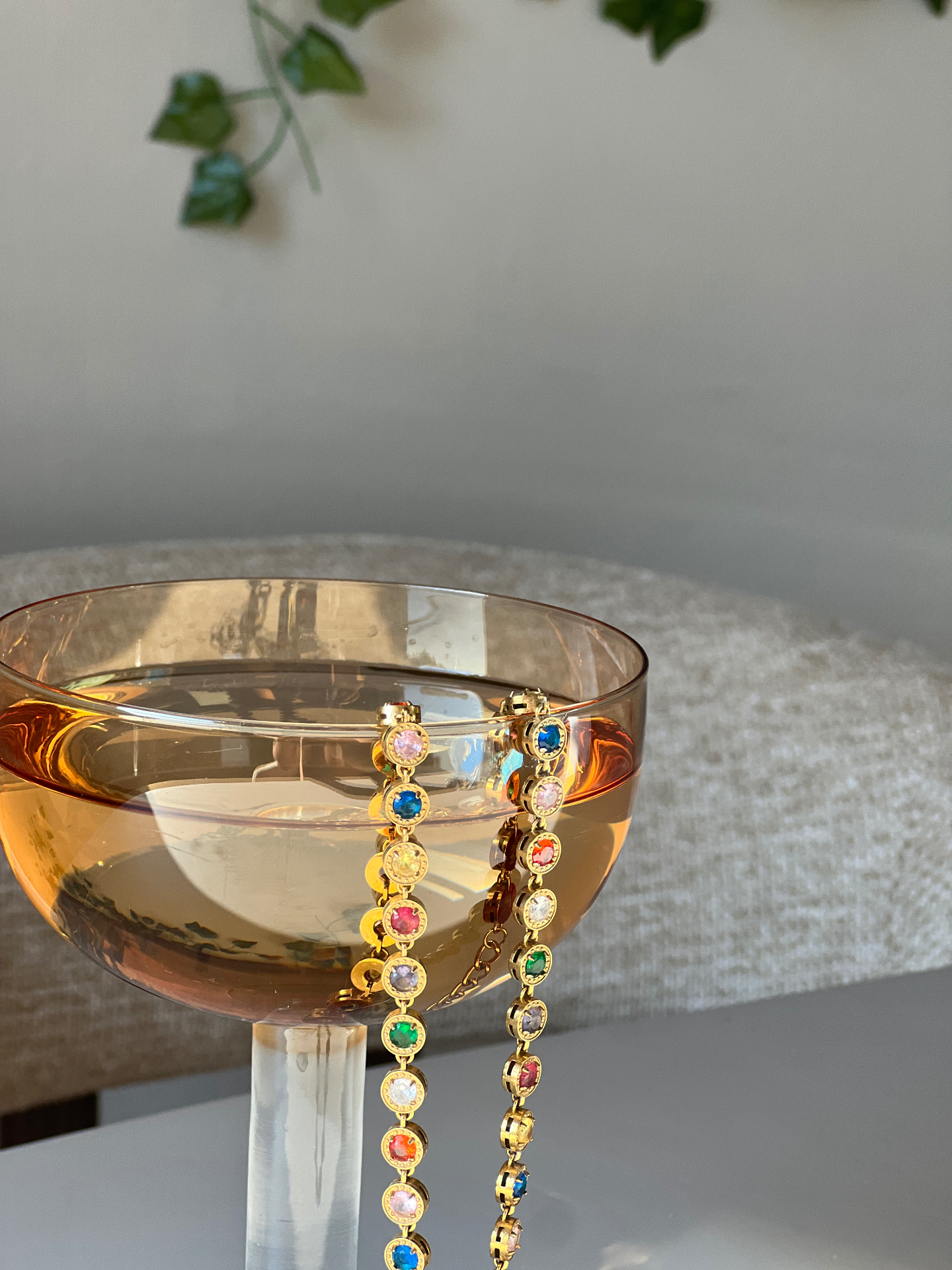 Gouden armband en ketting met gekleurde steentjes over een glas — waterproof sieraden van The Charm Bar